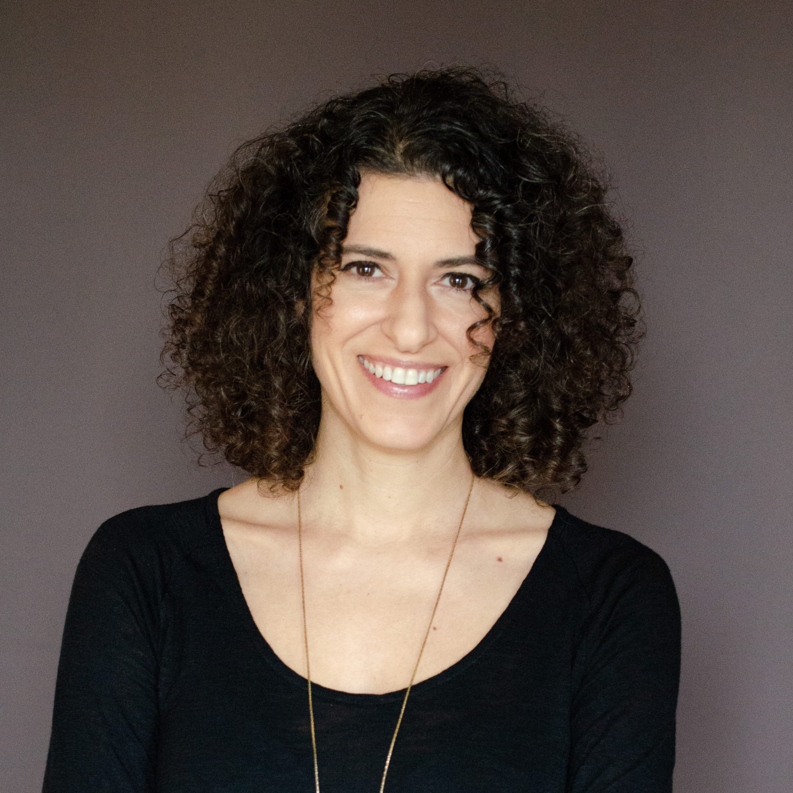 Woman with a black top and curly hair standing in front of a blank wall