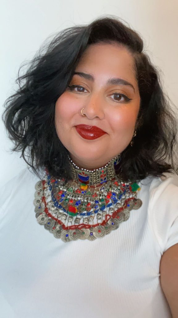 Selfie of a woman dressed in a white shirt, in front of a white wall.