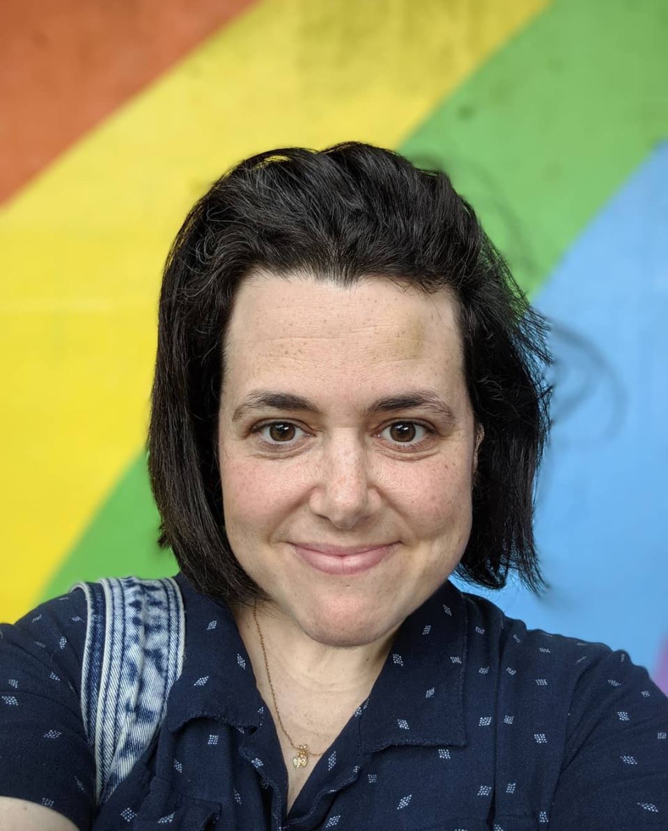 Woman with black hair standing in front of a colourful rainbow wall