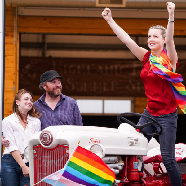 Dawn, her dad, and her tractor girl standing on a tractor while her parents look at her lovingly