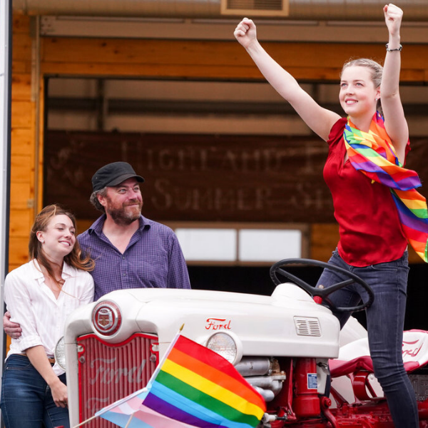 girl standing on a tractor while her parents look at her lovingly