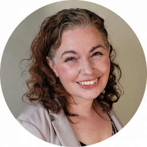 headshot of a woman in a cream coloured blazer smiling in front of a beige wall