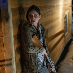 Don't Say It's Name Women standing against the wall holding a hunting gun