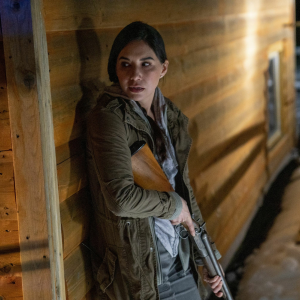 Women standing against the wall holding a hunting gun