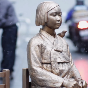 Bronze statue of a young asian girl sitting on a chair in the middle of a sidewalk