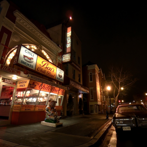 TRAVELING WHILE BLACK Image of a dark night street with bright shop signs