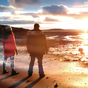 Image of two people standing at the edge of the beach watching a sunset
