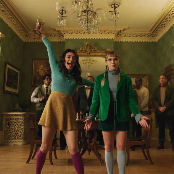 Two young girls standing in a foyer of an older looking home. One looks distressed while the other is jumping for joy.