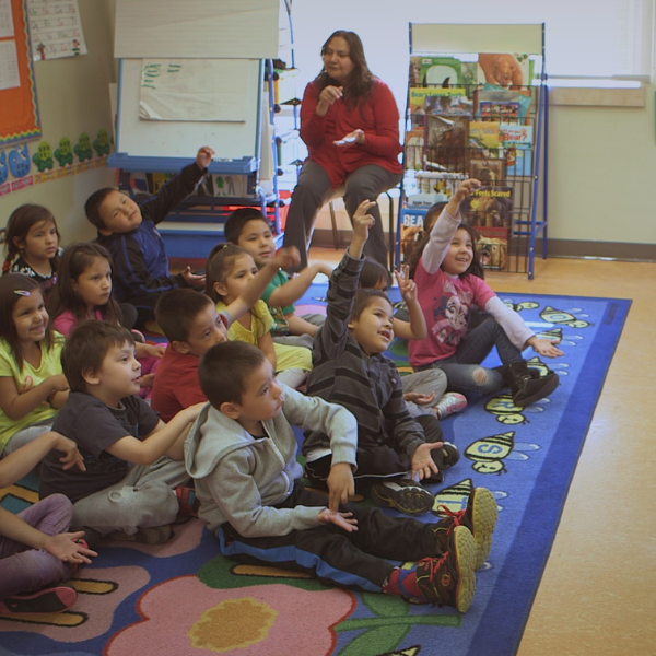 A group of young kindergarten students sit on a carpet in a classroom